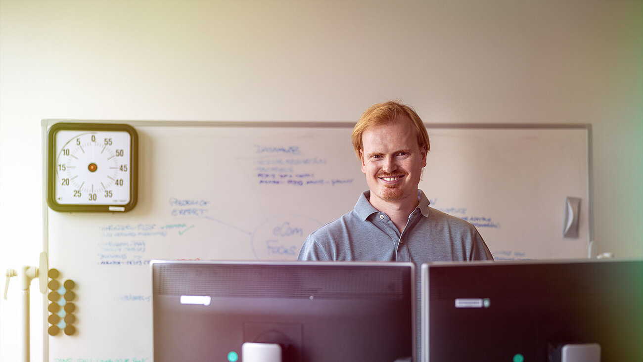 Ein Mann steht vor zwei Computermonitoren.