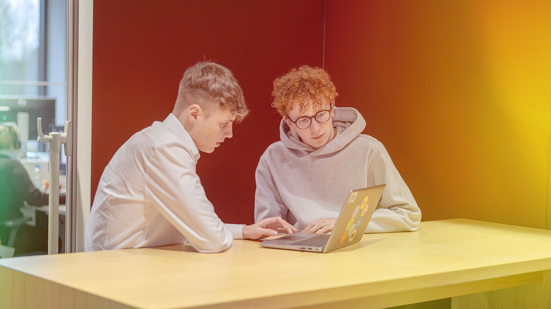 Zwei junge Männer sitzen an einem Tisch mit einem Laptop.